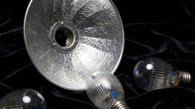 Three lightbulbs and a lamp shade on a fabric surface indoors