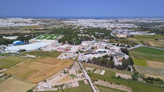 At Ta' Qali National Park in Malta, an aerial view shows the expansive green space bordered by Mediterranean countryside, fields, and nearby facilities including the Artisan Village.
