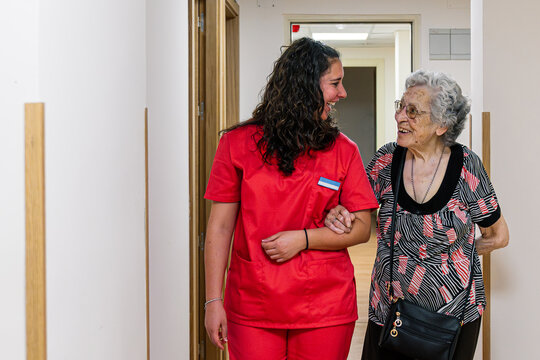 Nursing assistant providing compassionate support to an elderly patient walking down a hallway in a retirement care facility