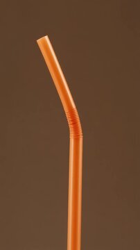 Close up of a flexible orange drinking straw on a brown background