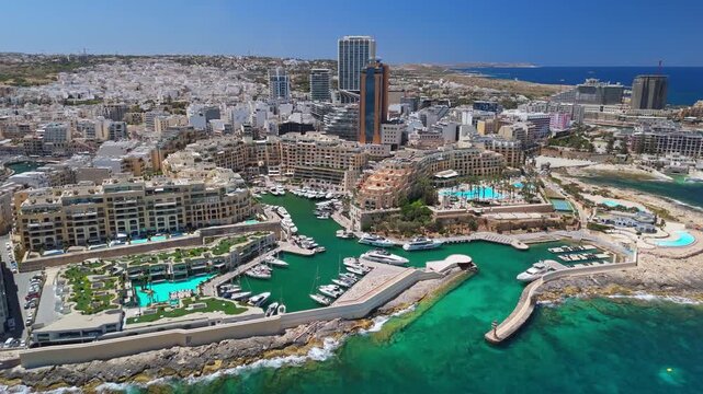 In St Julian's, Malta, Portomaso Marina with its yachts and surrounding high-rise buildings lines the Mediterranean coastline in a broad view captured from a drone.