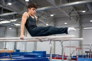 Fototapeta premium Male gymnast performing a routine on parallel bars inside a well-lit gymnasium with blue mats and equipment visible in the background