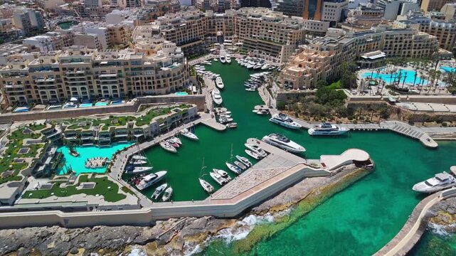 In St Julian's, Malta, boats and yachts line the clear green waters of Portomaso Marina beside modern Mediterranean architecture and waterfront residential buildings.