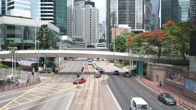 A bustling street scene in central Hong Kong features a dynamic mix of modern skyscrapers, iconic double-decker buses, and intricate tram tracks under an overcast sky. Hong Kong, China 20 May 2025