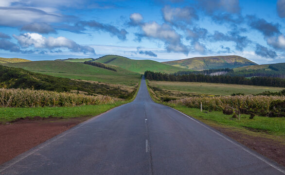 Perspectiva sim&eacute;trica de una carretera de asfalto vac&iacute;a que se extiende hacia el horizonte entre colinas verdes y llanuras rurales en la isla de Flores, Azores.
