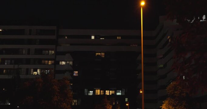 Night view of a modern residential apartment building with illuminated windows and warm street lighting. Contemporary urban housing complex under a dark evening sky in a quiet residential neighborhood