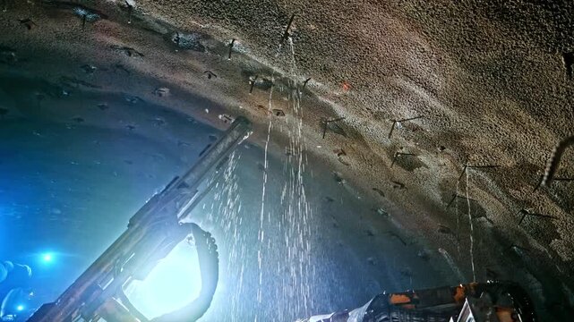 Tunnel jumbo drills the rock face inside an underground excavation, showing active tunnel construction, rock support preparation, heavy machinery and engineering work in a confined infrastructure site