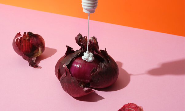 Peeling red onion with moisturiser being squeezed onto it from above 