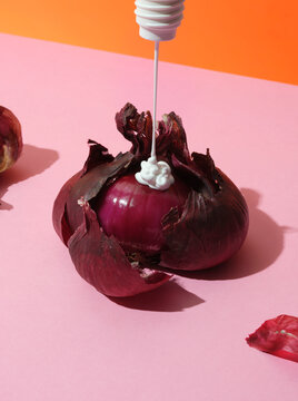 Peeling red onion with moisturiser being squeezed onto it from above 