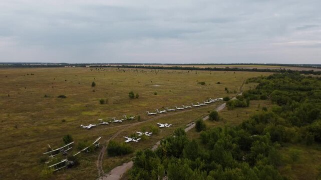 Aerial old abandoned airbase field with weathered hangar, helicopters and airplanes in summer greenery