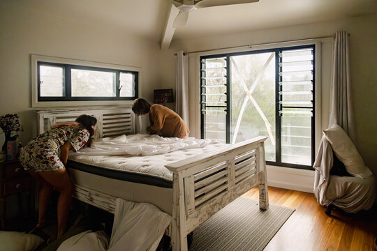 Sisters making bed beside taped window during storm