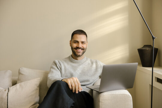 Man Sitting on Sofa With Laptop in Bright Room During Day Smiling