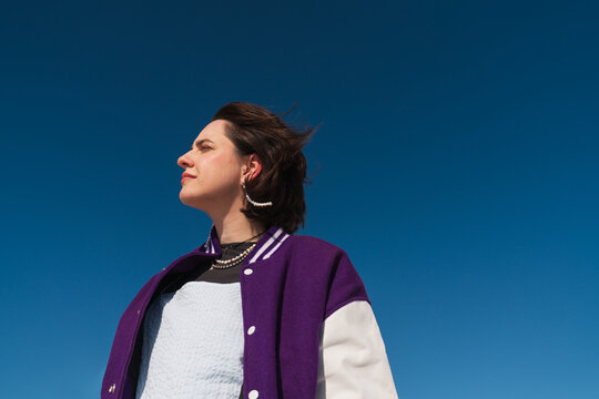 Woman in purple varsity jacket looking ahead under blue sky