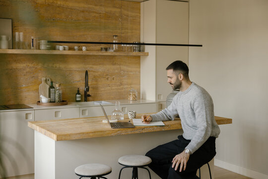 Man Working on Laptop at Kitchen Island in a Modern Home