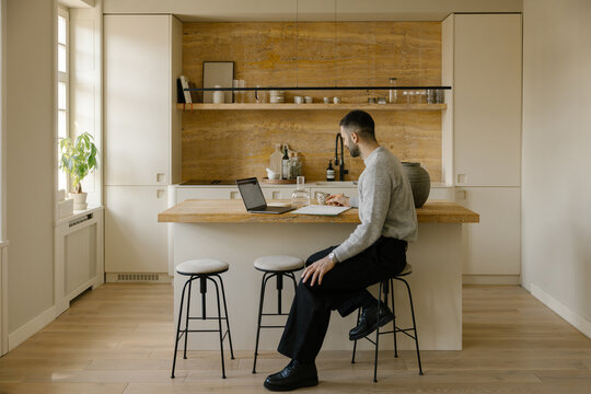 Man Working on Laptop at Kitchen Island in a Modern Home
