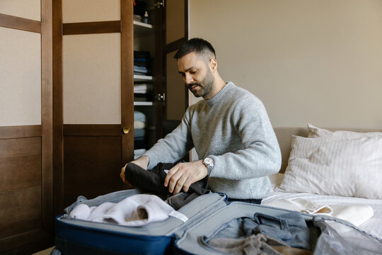 Man Packs Suitcase in Bedroom Before Trip
