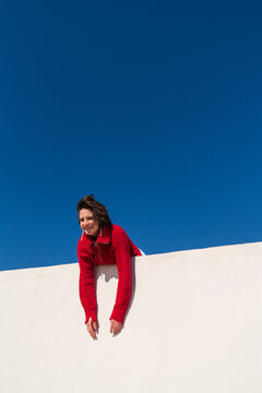 Woman in red sweater leaning over parapet under blue sky