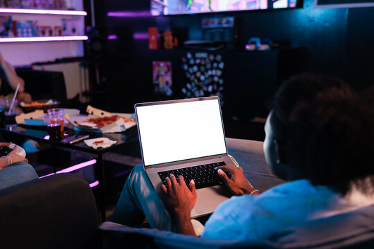 Man using laptop while friends gather in neon-lit lounge