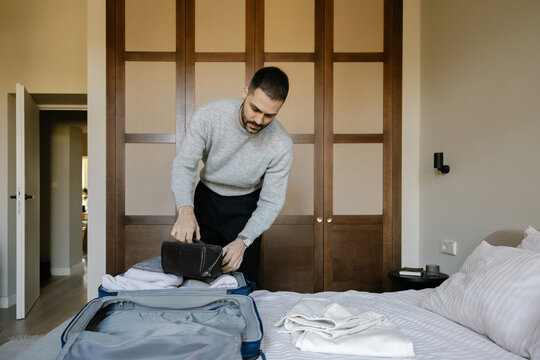 Man Packs Suitcase in Hotel Room on Bed