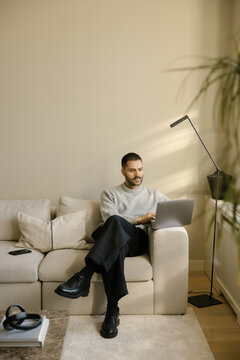 Man Using Laptop While Sitting on Sofa in Bright Room