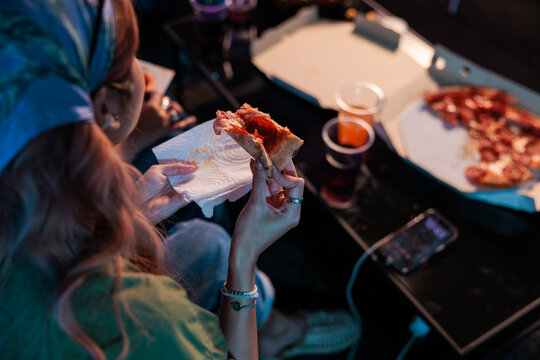 Woman eating pizza and drinking soda in the dark.