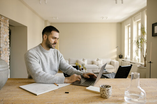 Man Works on Laptop at Table in Modern Living Room During Daytime