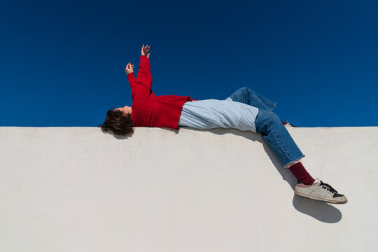 Woman in red sweater lying on parapet under blue sky