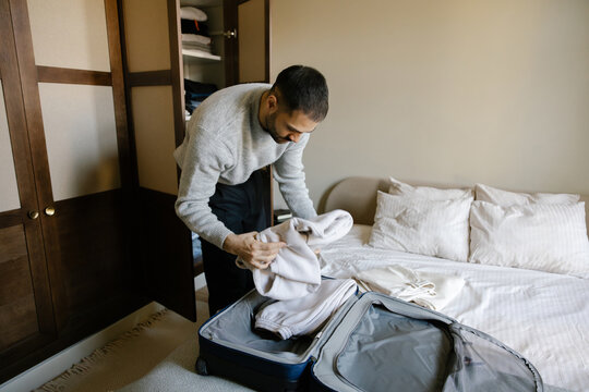 Man Packing Clothes Into Suitcase in a Bedroom on Bed