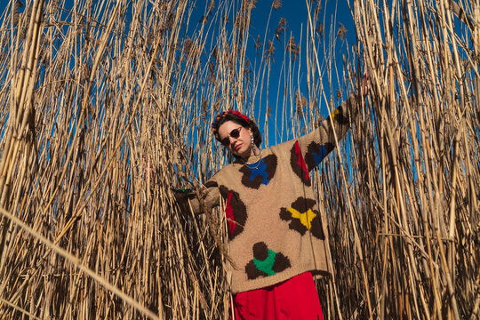 Woman posing among tall dry reeds wearing colorful sweater