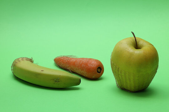 Still life with banana, apple and carrot, parts of which are in metal wire mesh. Close-up with great depth of field on light background.