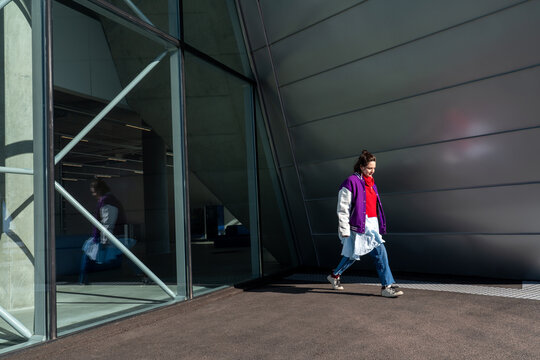 Woman walking near modern glass and metal building exterior