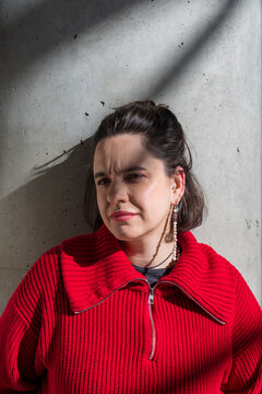 Woman in red sweater standing against concrete wall in sunlight