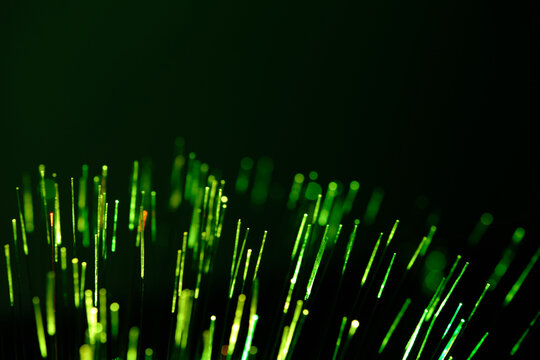 Radiant green fiber optic tips glow intensely, cutting through solid dark backdrop.
