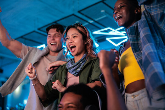 Friends celebrate a win, illuminated by blue neon lights.