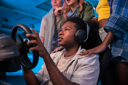Friends watch intently as a young man plays racing game.