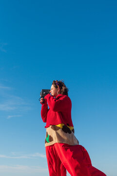Person filming with camcorder wearing red outfit under blue sky