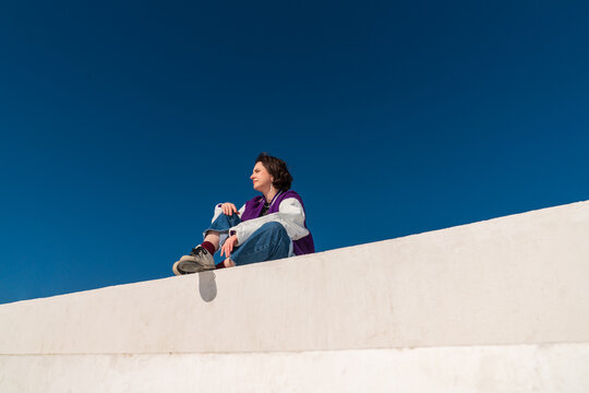 Woman in jacket sitting on wall looking into distance