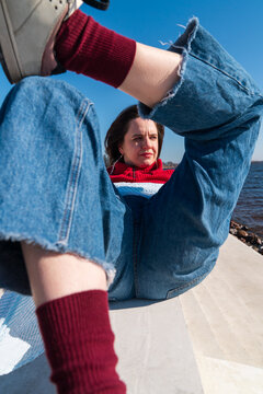 Low angle view of woman in red sweater with legs raised by waterfront