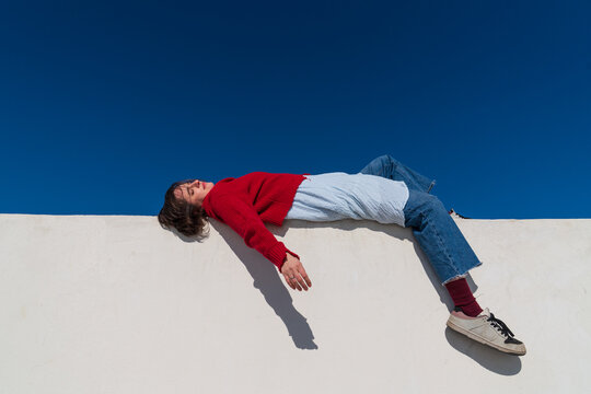 Woman in red sweater lying on wall under blue sky