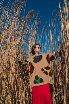 Woman in colorful sweater posing among tall reeds under blue sky
