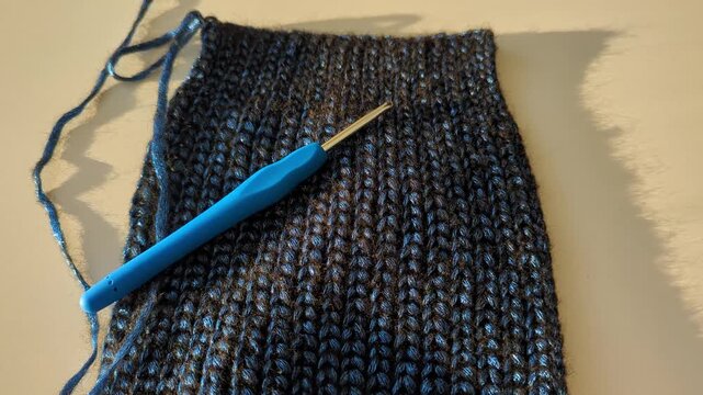 Blue crochet hook on dark shiny textured warm winter crochet project in soft lighting