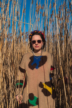 Woman in sweater and sunglasses standing in tall reeds portrait