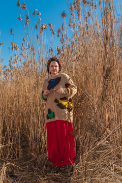Woman in  sweater and red skirt standing among tall dry reeds