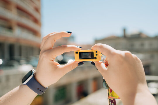 Person Holding Tiny Camera Against Bright Urban Background