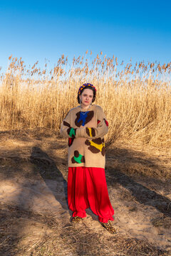 Woman in colorful outfit standing on sandy path near dry reeds