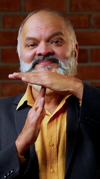 Indian senior businessman or corporate executive gesturing a time out with his hands signaling for a break or a stop in proceedings while standing against a red brick wall in a cozy moody office