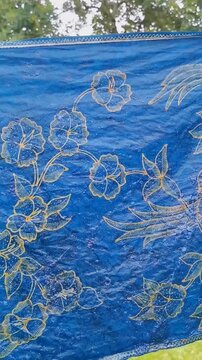 Vertical video of Indonesian traditional indigo batik tulis textile drying outdoors. Handmade fabric crafted with natural dye, artisan craftsmanship, cultural heritage and sustainable textiles. 
