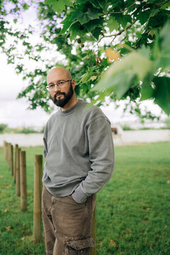 Bald bearded man standing under green tree outdoors