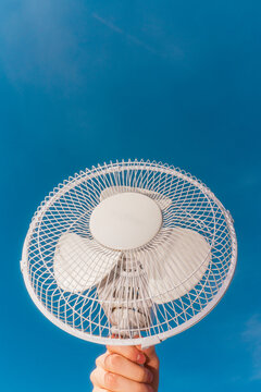 Hand holding portable electric fan against blue sky