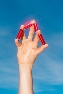 Hand balancing red alkaline batteries against blue sky